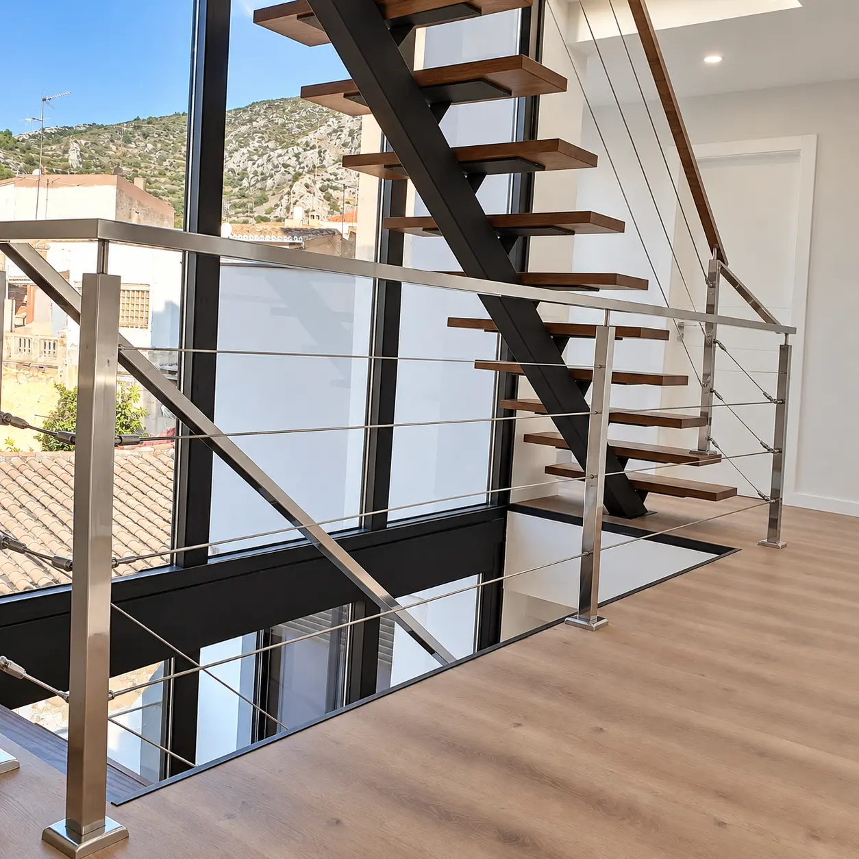 Escalera de estructura central oscura y peldaños de madera junto a un ventanal