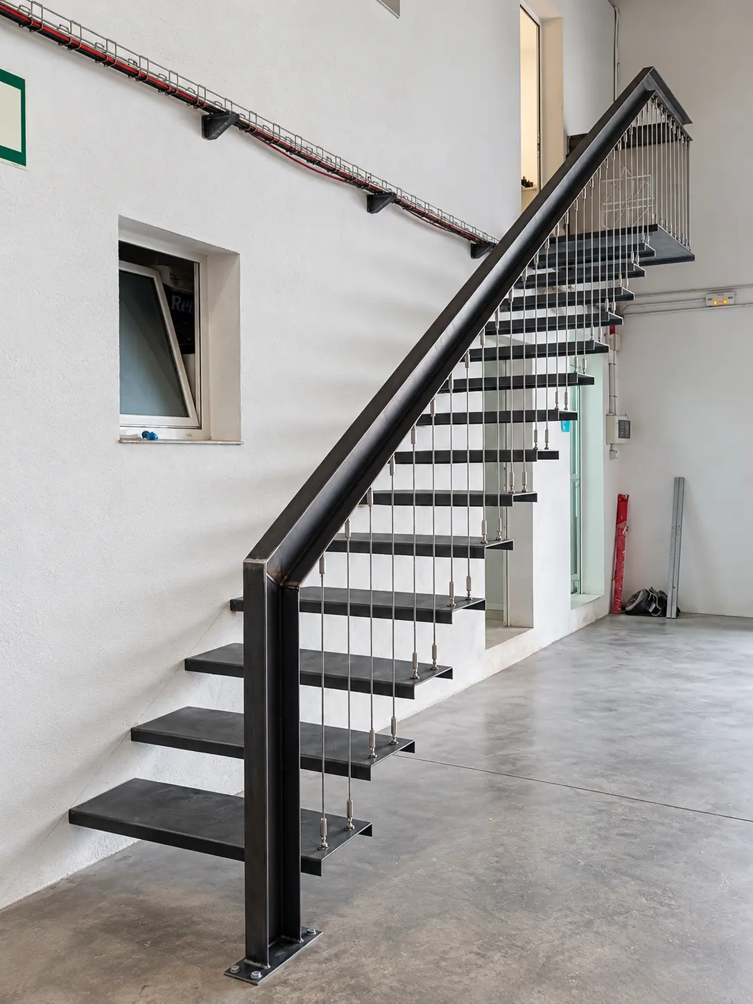 Escalera metálica de peldaños abiertos con barandilla de cables verticales