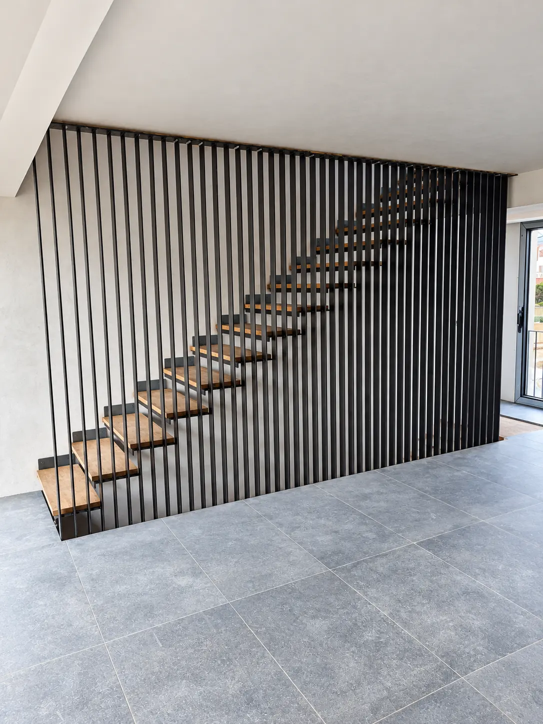 Escalera de peldaños de madera delimitada por barras metálicas negras de suelo a techo